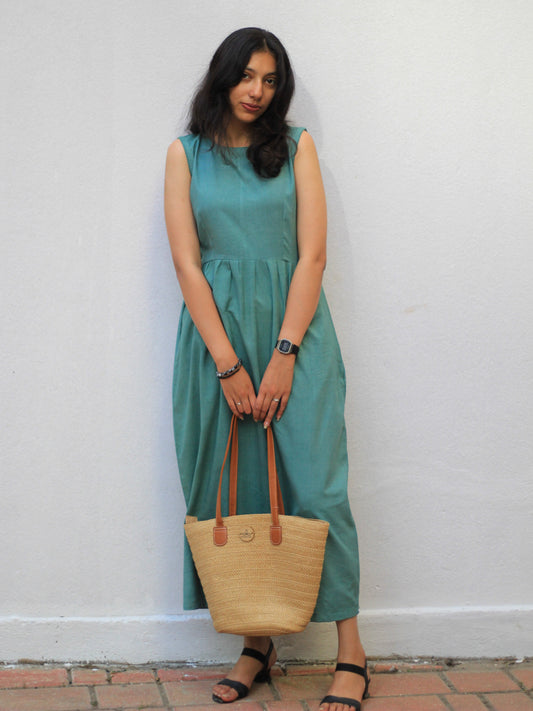 Model wearing Evara’s Dewy Meadow Sleeveless Dress, crafted from a premium blend of banana fiber and cotton. This elegant midi dress in a sea green hue features a sleeveless design, a flattering gathered waist, and functional side pockets for convenience. A subtle back slit adds ease of movement, making it a perfect blend of style and comfort. Designed for consumers who appreciate natural fabrics and timeless fashion. Shop clothing at Evara.