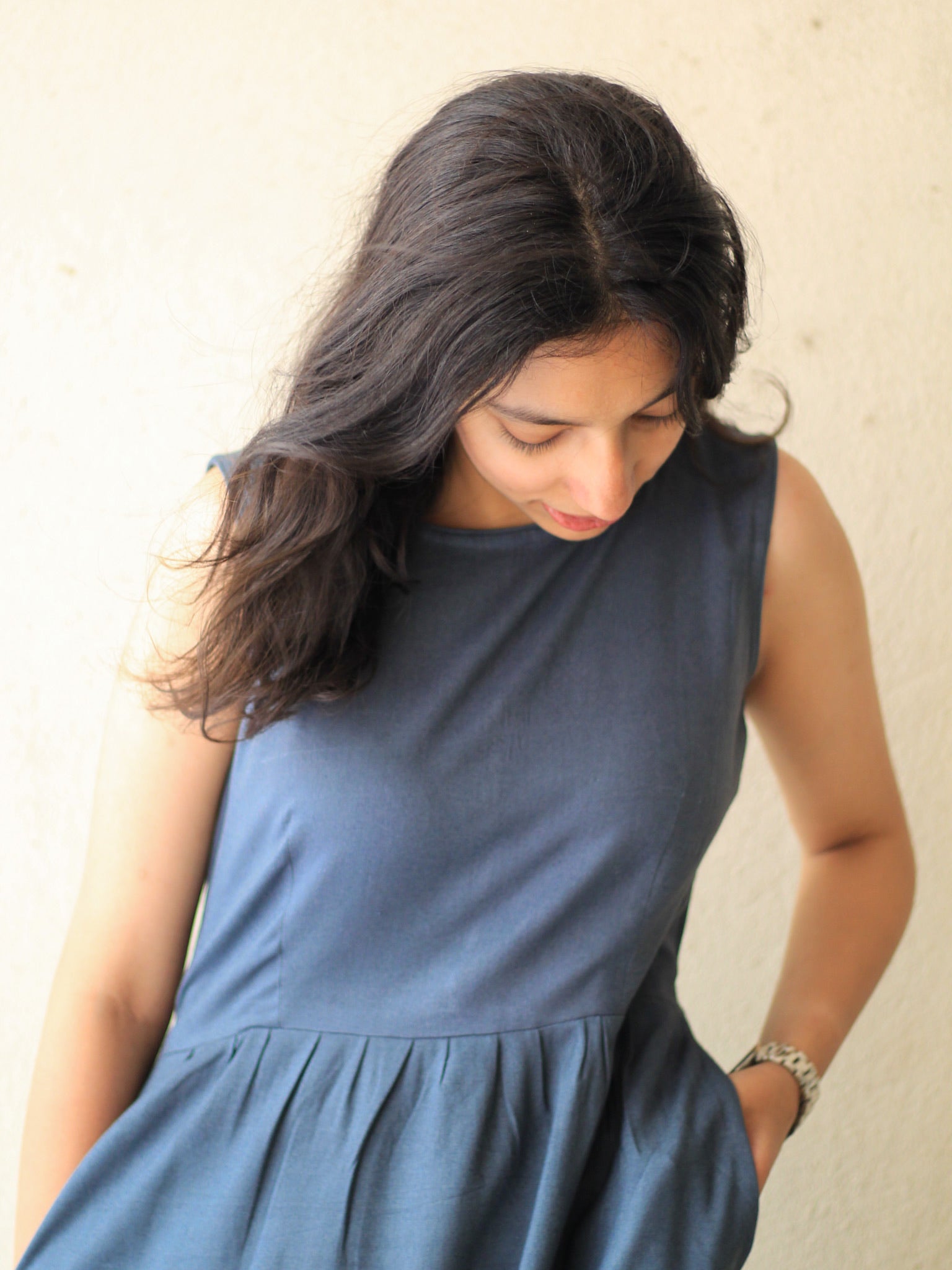 Model wearing Evara’s Cosmic Dusk Sleeveless Dress, crafted from a premium blend of banana fiber and cotton. This elegant midi dress in a deep dusk blue hue features a sleeveless design, a flattering gathered waist, and functional side pockets for convenience. A subtle back slit adds ease of movement, making it a perfect blend of style and comfort. Designed for consumers who appreciate natural fabrics and timeless fashion. Shop clothing at Evara.