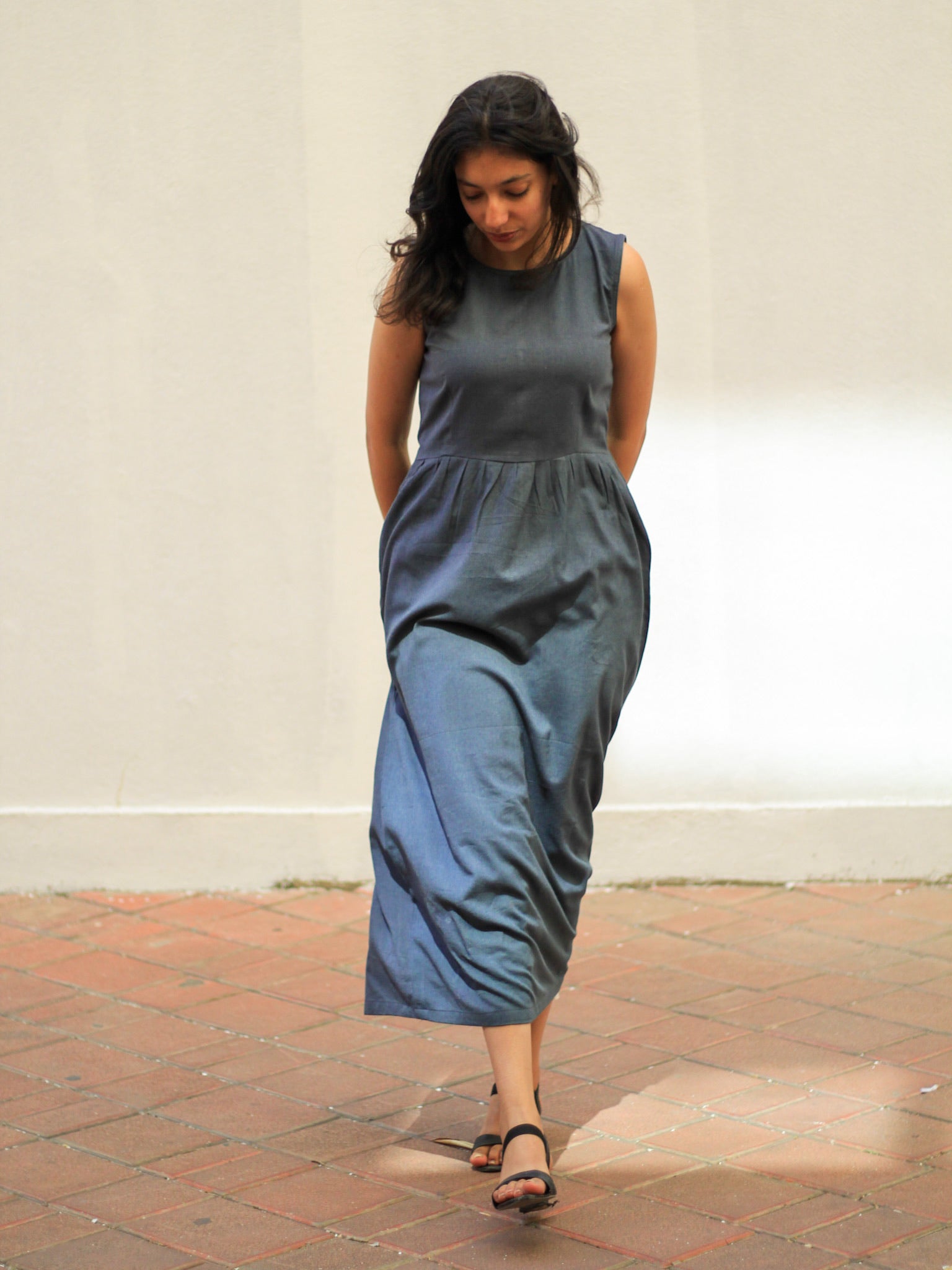 Model wearing Evara’s Cosmic Dusk Sleeveless Dress, crafted from a premium blend of banana fiber and cotton. This elegant midi dress in a deep dusk blue hue features a sleeveless design, a flattering gathered waist, and functional side pockets for convenience. A subtle back slit adds ease of movement, making it a perfect blend of style and comfort. Designed for consumers who appreciate natural fabrics and timeless fashion. Shop clothing at Evara.