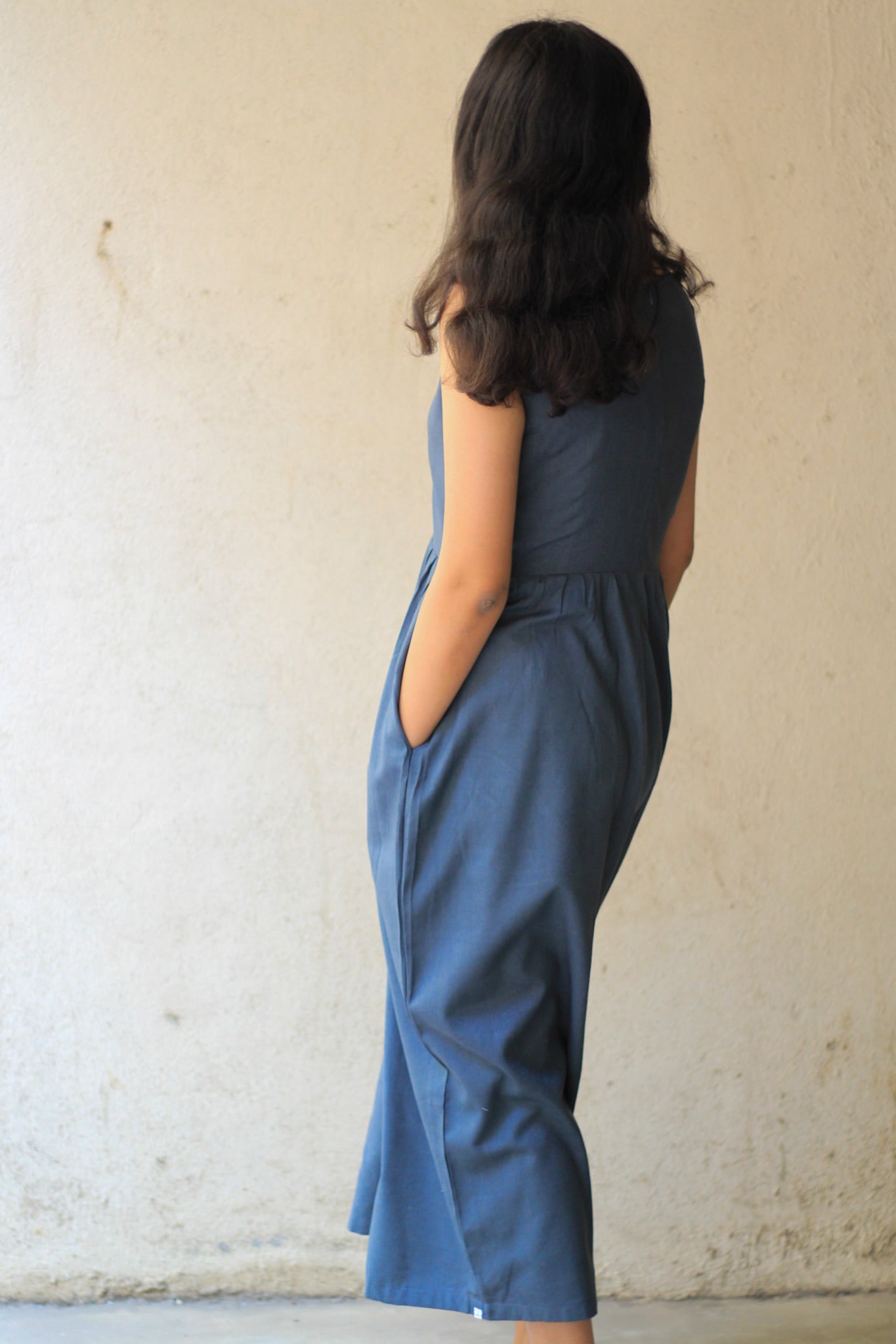 Model wearing Evara’s Cosmic Dusk Sleeveless Dress, crafted from a premium blend of banana fiber and cotton. This elegant midi dress in a deep dusk blue hue features a sleeveless design, a flattering gathered waist, and functional side pockets for convenience. A subtle back slit adds ease of movement, making it a perfect blend of style and comfort. Designed for consumers who appreciate natural fabrics and timeless fashion. Shop clothing at Evara.