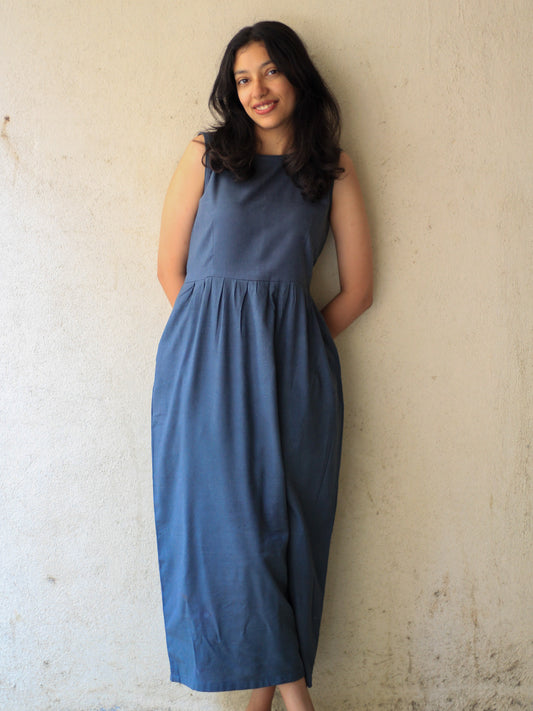 Model wearing Evara’s Cosmic Dusk Sleeveless Dress, crafted from a premium blend of banana fiber and cotton. This elegant midi dress in a deep dusk blue hue features a sleeveless design, a flattering gathered waist, and functional side pockets for convenience. A subtle back slit adds ease of movement, making it a perfect blend of style and comfort. Designed for consumers who appreciate natural fabrics and timeless fashion. Shop clothing at Evara.