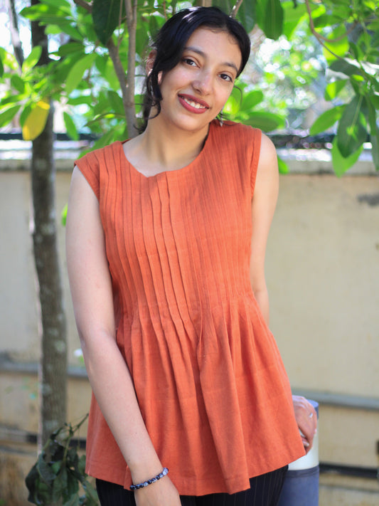 Model wearing Evara’s Rust Reverie Sleeveless Pleated Top, crafted from a sustainable blend of banana fiber and cotton. This airy light blue top features a sleeveless design, fine vertical pleats on the bodice, and a softly flared hem that offers a relaxed yet refined silhouette. Perfect for warm-weather layering or standalone elegance, it blends comfort with conscious fashion. Designed for consumers who value eco-friendly fabrics and contemporary, timeless style. Shop clothing at Evara.