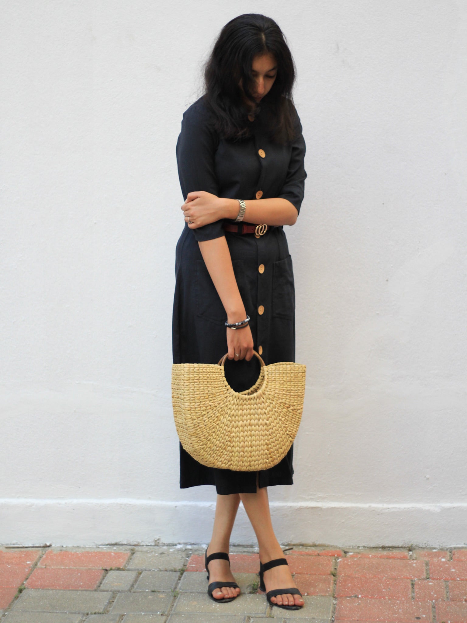 Model wearing Evara’s Obsidian Noir Button-Down Dress, crafted from a premium blend of banana fiber and cotton. This timeless black midi dress features a structured silhouette, three-quarter sleeves, a classic button-down front, and functional patch pockets. Styled with a belt for a defined waist, it offers effortless sophistication for work or casual outings. Designed for consumers who appreciate natural fabrics and timeless fashion. Shop clothing at Evara.