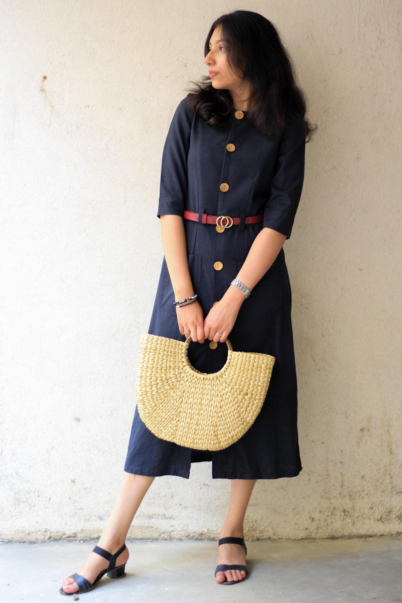 Model wearing Evara’s Obsidian Noir Button-Down Dress, crafted from a premium blend of banana fiber and cotton. This timeless black midi dress features a structured silhouette, three-quarter sleeves, a classic button-down front, and functional patch pockets. Styled with a belt for a defined waist, it offers effortless sophistication for work or casual outings. Designed for consumers who appreciate natural fabrics and timeless fashion. Shop clothing at Evara.