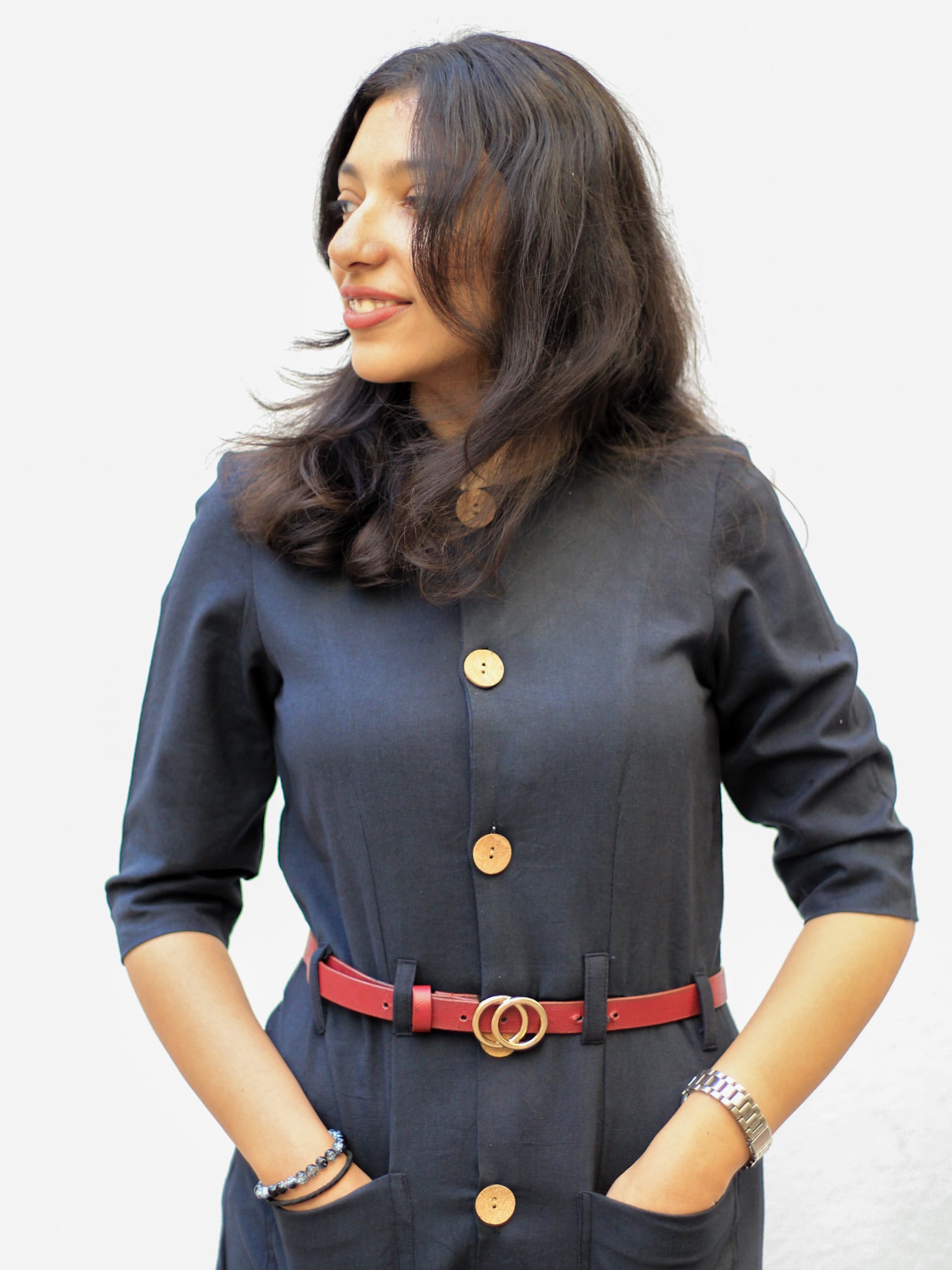 Model wearing Evara’s Obsidian Noir Button-Down Dress, crafted from a premium blend of banana fiber and cotton. This timeless black midi dress features a structured silhouette, three-quarter sleeves, a classic button-down front, and functional patch pockets. Styled with a belt for a defined waist, it offers effortless sophistication for work or casual outings. Designed for consumers who appreciate natural fabrics and timeless fashion. Shop clothing at Evara.