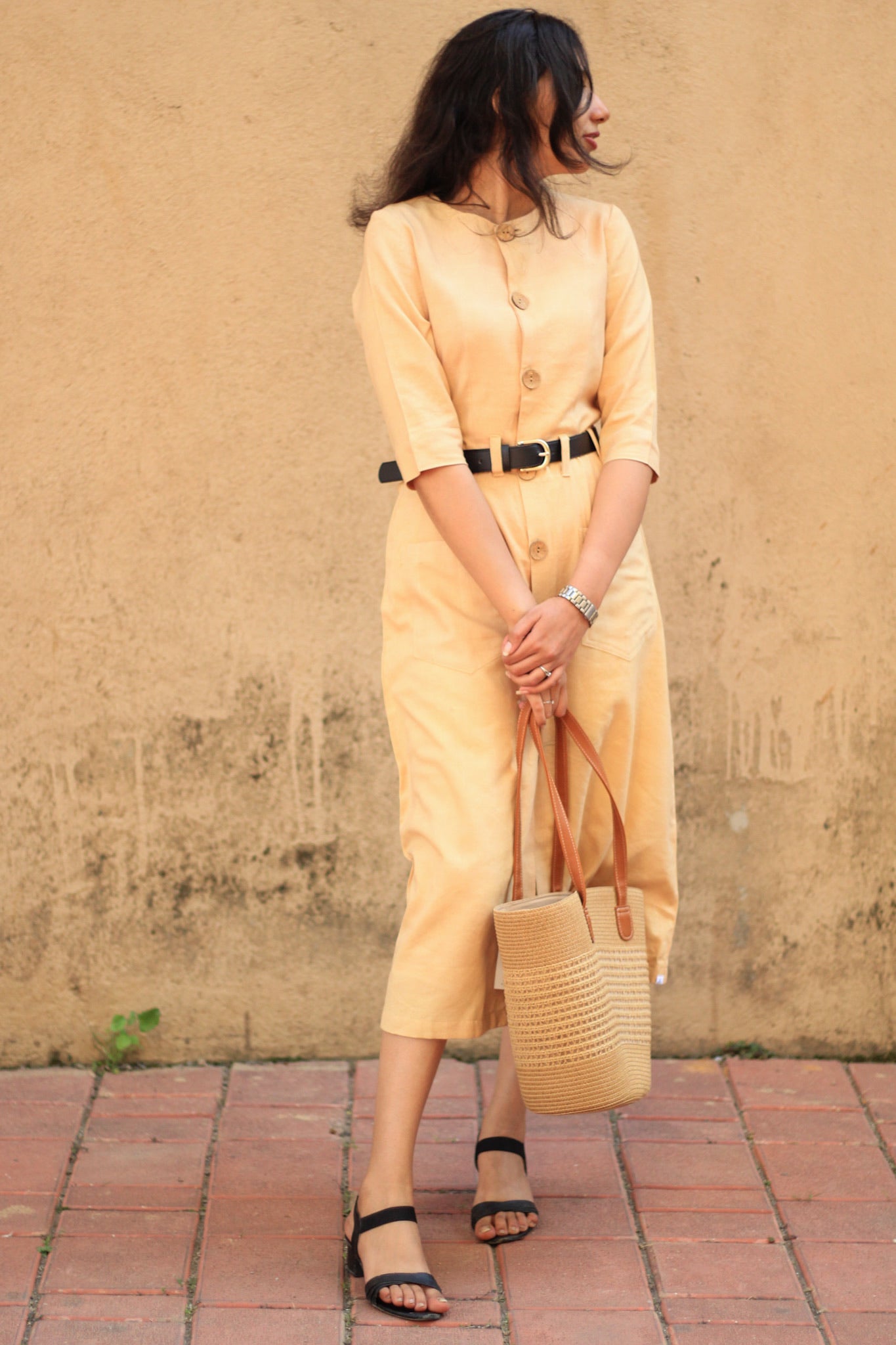 Model wearing Evara’s Golden Aura Button-Down Dress, crafted from a premium blend of banana fiber and cotton. This elegant midi dress in a warm golden hue features a structured silhouette, three-quarter sleeves, a classic button-down front, and functional patch pockets. Styled with a belt for a defined waist, it offers effortless sophistication for work or casual outings. Designed for consumers who appreciate natural fabrics and timeless fashion. Shop clothing at Evara.