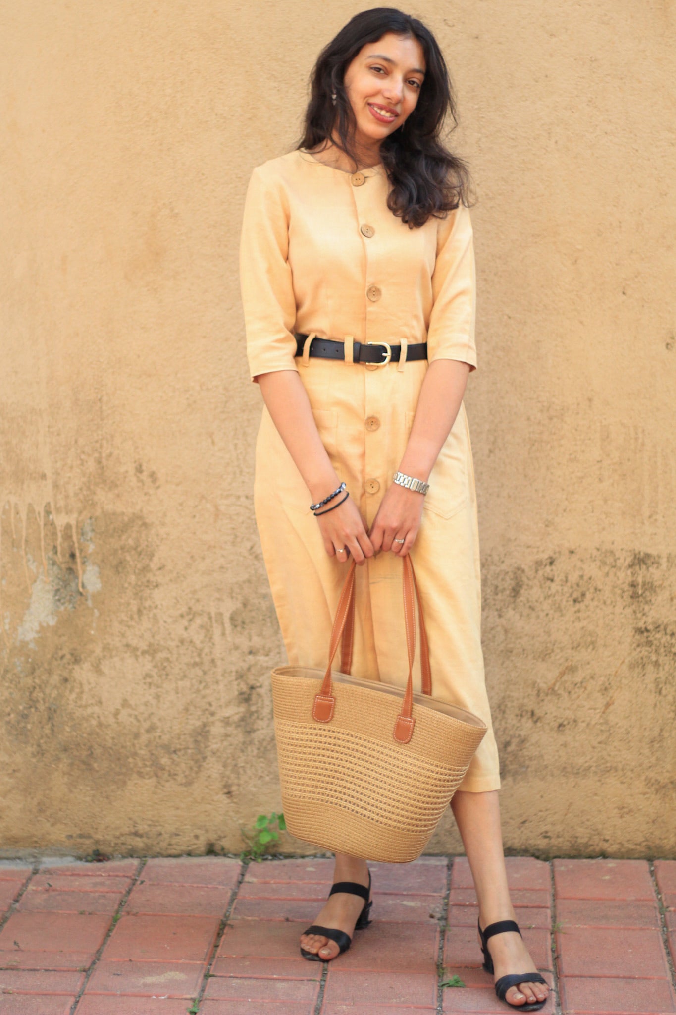 Model wearing Evara’s Golden Aura Button-Down Dress, crafted from a premium blend of banana fiber and cotton. This elegant midi dress in a warm golden hue features a structured silhouette, three-quarter sleeves, a classic button-down front, and functional patch pockets. Styled with a belt for a defined waist, it offers effortless sophistication for work or casual outings. Designed for consumers who appreciate natural fabrics and timeless fashion. Shop clothing at Evara.
