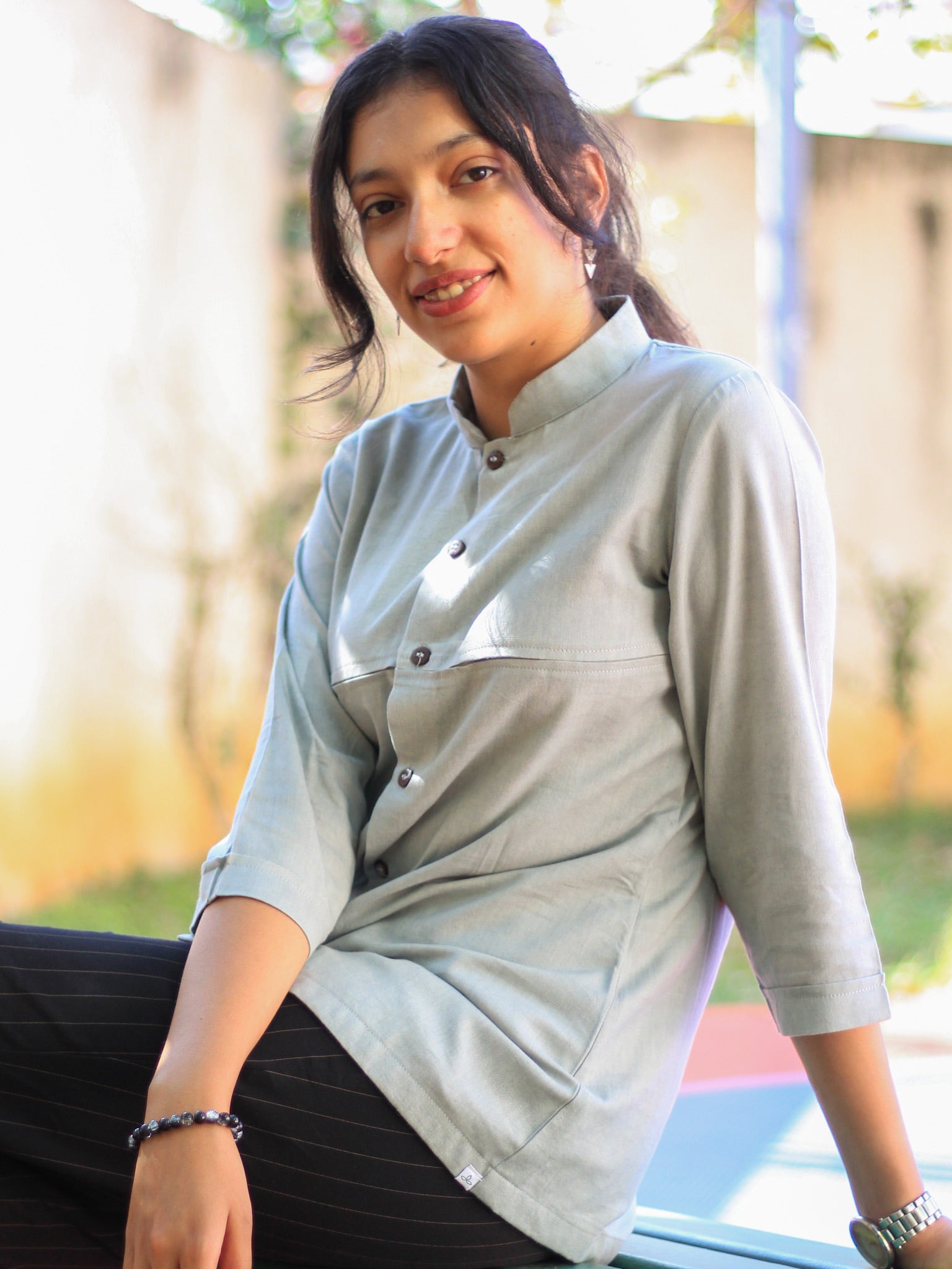 Model wearing Evara’s Smoky Pearl Button-Down Shirt, crafted from a premium blend of banana fiber and cotton. This elegant three-quarter sleeve shirt in a grey hue features a mandarin collar, a structured yet relaxed fit, and a stylish button-down front. Designed for effortless versatility, it pairs perfectly with both formal and casual looks. Designed for consumers who appreciate natural fabrics and timeless fashion. Shop clothing at Evara.