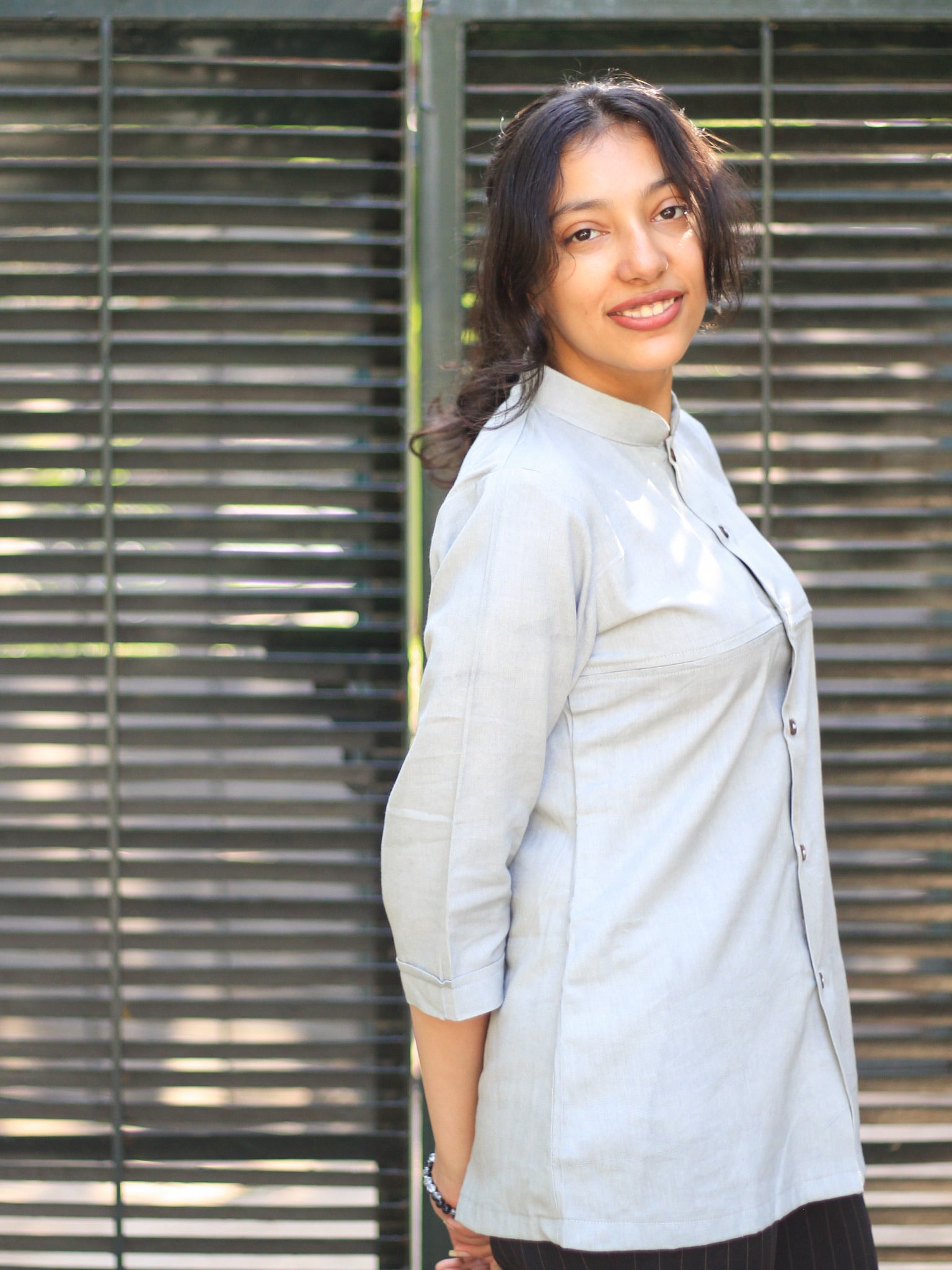 Model wearing Evara’s Smoky Pearl Button-Down Shirt, crafted from a premium blend of banana fiber and cotton. This elegant three-quarter sleeve shirt in a grey hue features a mandarin collar, a structured yet relaxed fit, and a stylish button-down front. Designed for effortless versatility, it pairs perfectly with both formal and casual looks. Designed for consumers who appreciate natural fabrics and timeless fashion. Shop clothing at Evara.