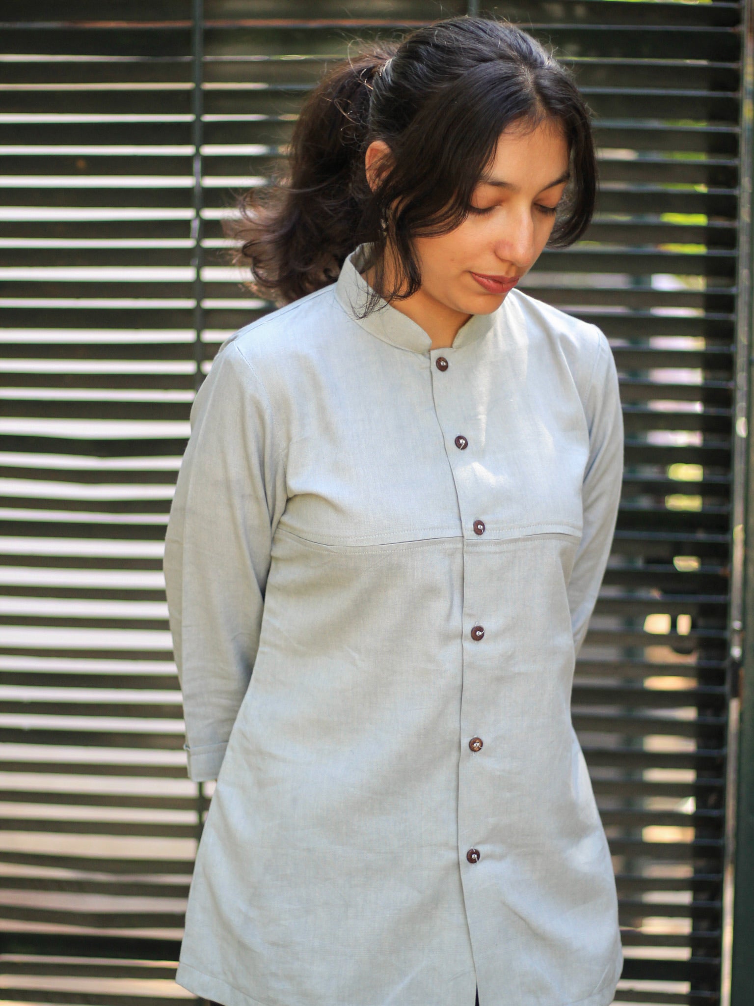 Model wearing Evara’s Smoky Pearl Button-Down Shirt, crafted from a premium blend of banana fiber and cotton. This elegant three-quarter sleeve shirt in a grey hue features a mandarin collar, a structured yet relaxed fit, and a stylish button-down front. Designed for effortless versatility, it pairs perfectly with both formal and casual looks. Designed for consumers who appreciate natural fabrics and timeless fashion. Shop clothing at Evara.
