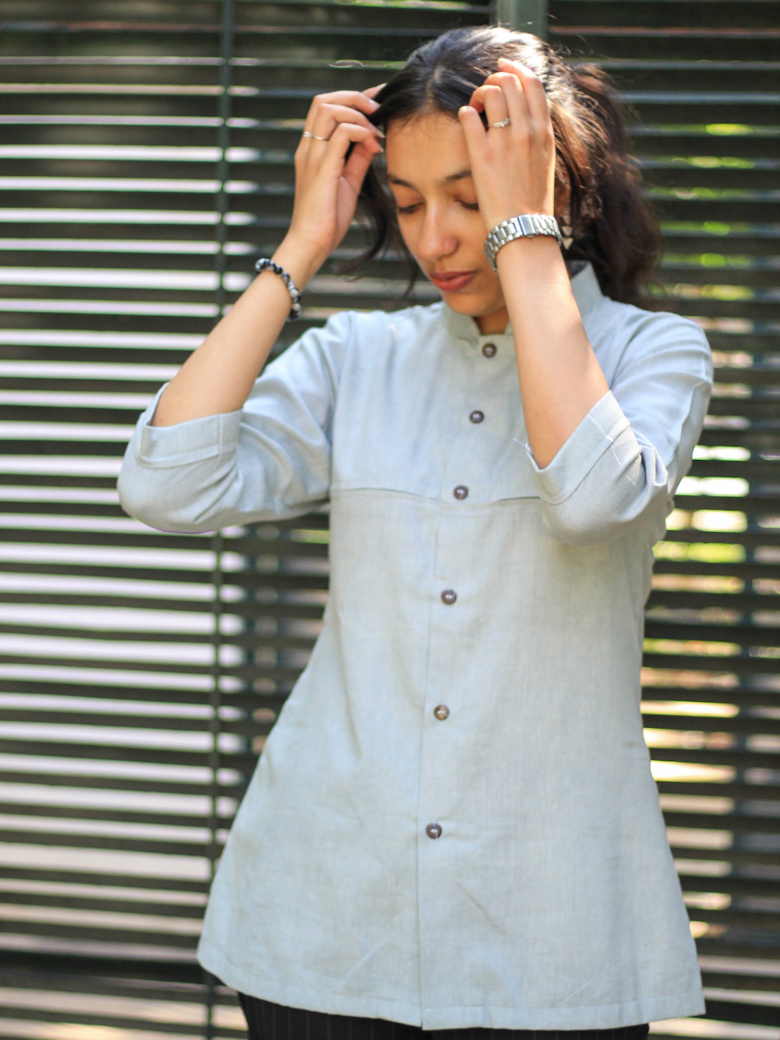 Model wearing Evara’s Smoky Pearl Button-Down Shirt, crafted from a premium blend of banana fiber and cotton. This elegant three-quarter sleeve shirt in a grey hue features a mandarin collar, a structured yet relaxed fit, and a stylish button-down front. Designed for effortless versatility, it pairs perfectly with both formal and casual looks. Designed for consumers who appreciate natural fabrics and timeless fashion. Shop clothing at Evara.