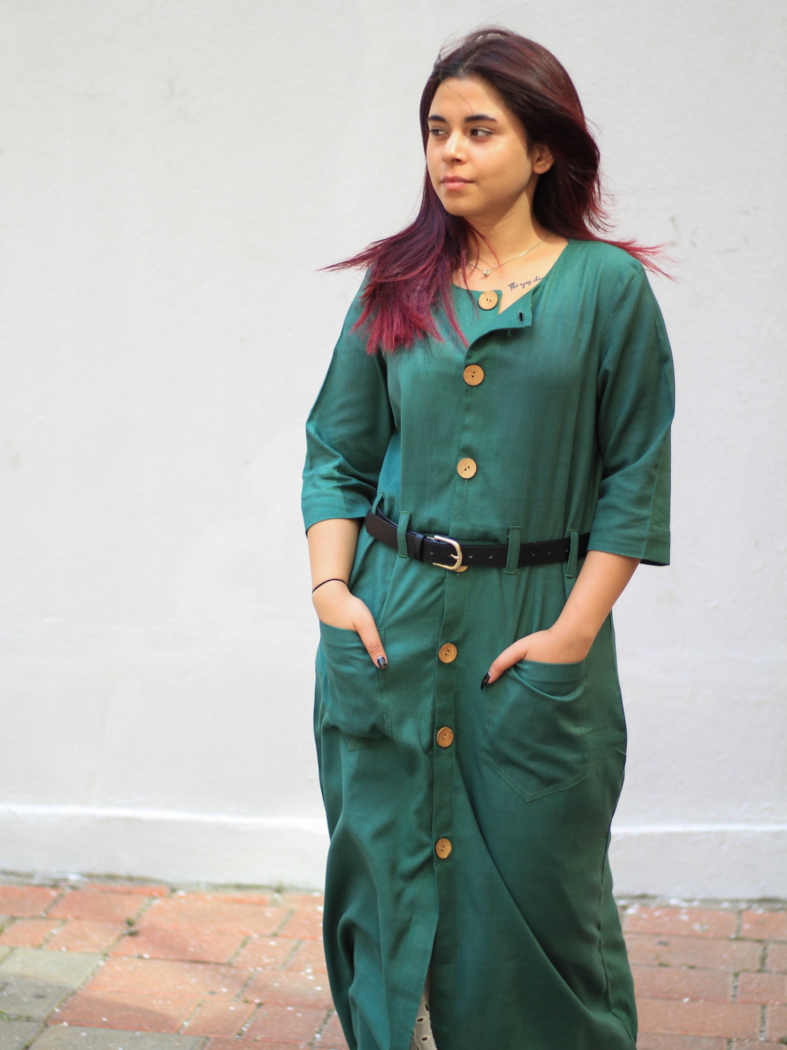 Model wearing Evara’s Botanic Luxe Button-Down Dress, crafted from a premium blend of banana fiber and cotton. This elegant midi dress in a green hue features a structured silhouette, three-quarter sleeves, a classic button-down front, and functional patch pockets. Styled with a belt for a defined waist, it offers effortless sophistication for work or casual outings. Designed for consumers who appreciate natural fabrics and timeless fashion. Shop clothing at Evara.