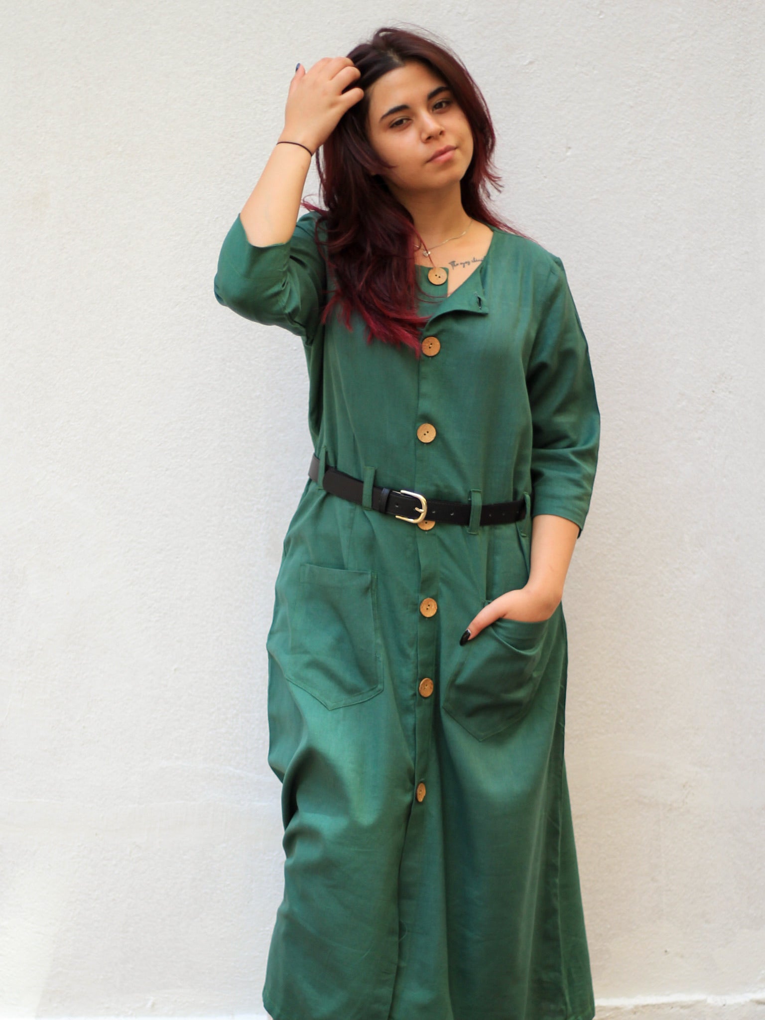 Model wearing Evara’s Botanic Luxe Button-Down Dress, crafted from a premium blend of banana fiber and cotton. This elegant midi dress in a green hue features a structured silhouette, three-quarter sleeves, a classic button-down front, and functional patch pockets. Styled with a belt for a defined waist, it offers effortless sophistication for work or casual outings. Designed for consumers who appreciate natural fabrics and timeless fashion. Shop clothing at Evara.