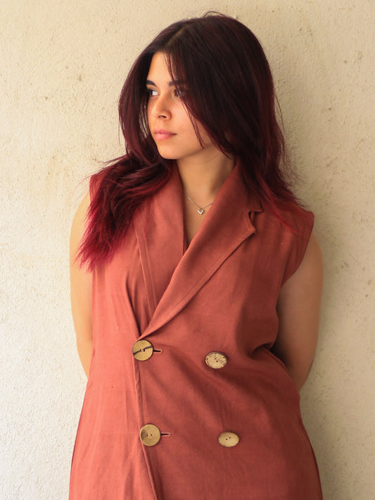 Model wearing Evara’s Maple Muse Sleeveless Blazer Dress, crafted from a breathable blend of cotton and banana fiber. This elegant, ankle-length dress features a sharp tailored silhouette, a sleek lapel collar, and a sleeveless design that balances structure with graceful fluidity. Naturally textured and lightweight, the fabric offers all-day comfort with elevated style. Perfect for power dressing or evening occasions. Discover eco-friendly clothing at Evara.