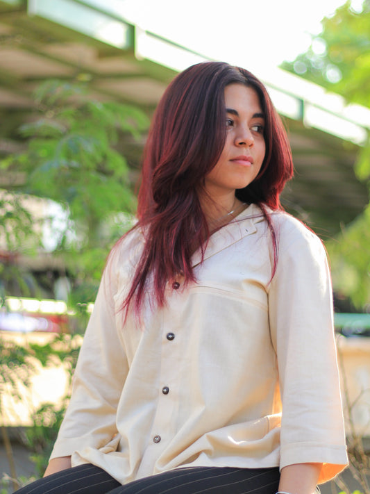 Model wearing Evara’s Buttercream Bliss Button-Down Shirt, crafted from a premium blend of banana fiber and cotton. This elegant three-quarter sleeve shirt in a golden hue features a mandarin collar, a structured yet relaxed fit, and a stylish button-down front. Designed for effortless versatility, it pairs perfectly with both formal and casual looks. Designed for consumers who appreciate natural fabrics and timeless fashion. Shop clothing at Evara.