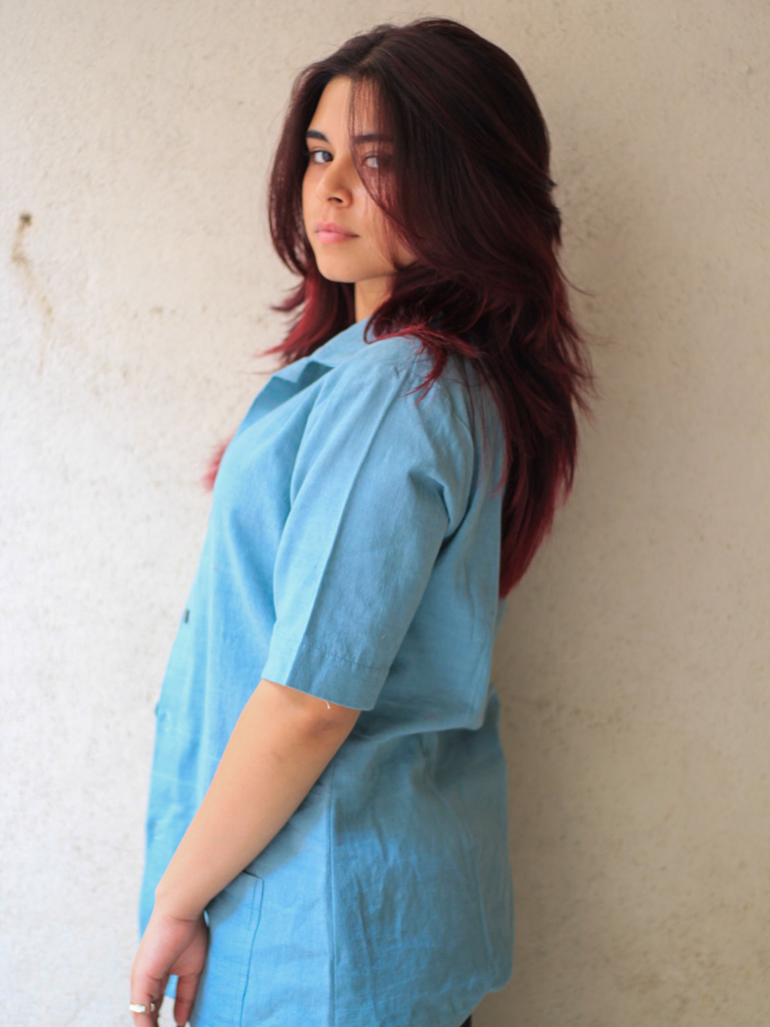 Model wearing Evara’s Aqua Petal Half-Sleeve Button-Down Shirt, made from a sustainable blend of banana fiber and cotton. This lightweight, breathable shirt features a structured silhouette, soft texture, and natural sheen, offering all-day comfort with moisture-wicking properties. A versatile wardrobe staple, ideal for casual and smart-casual looks. Shop eco-friendly fashion at Evara.