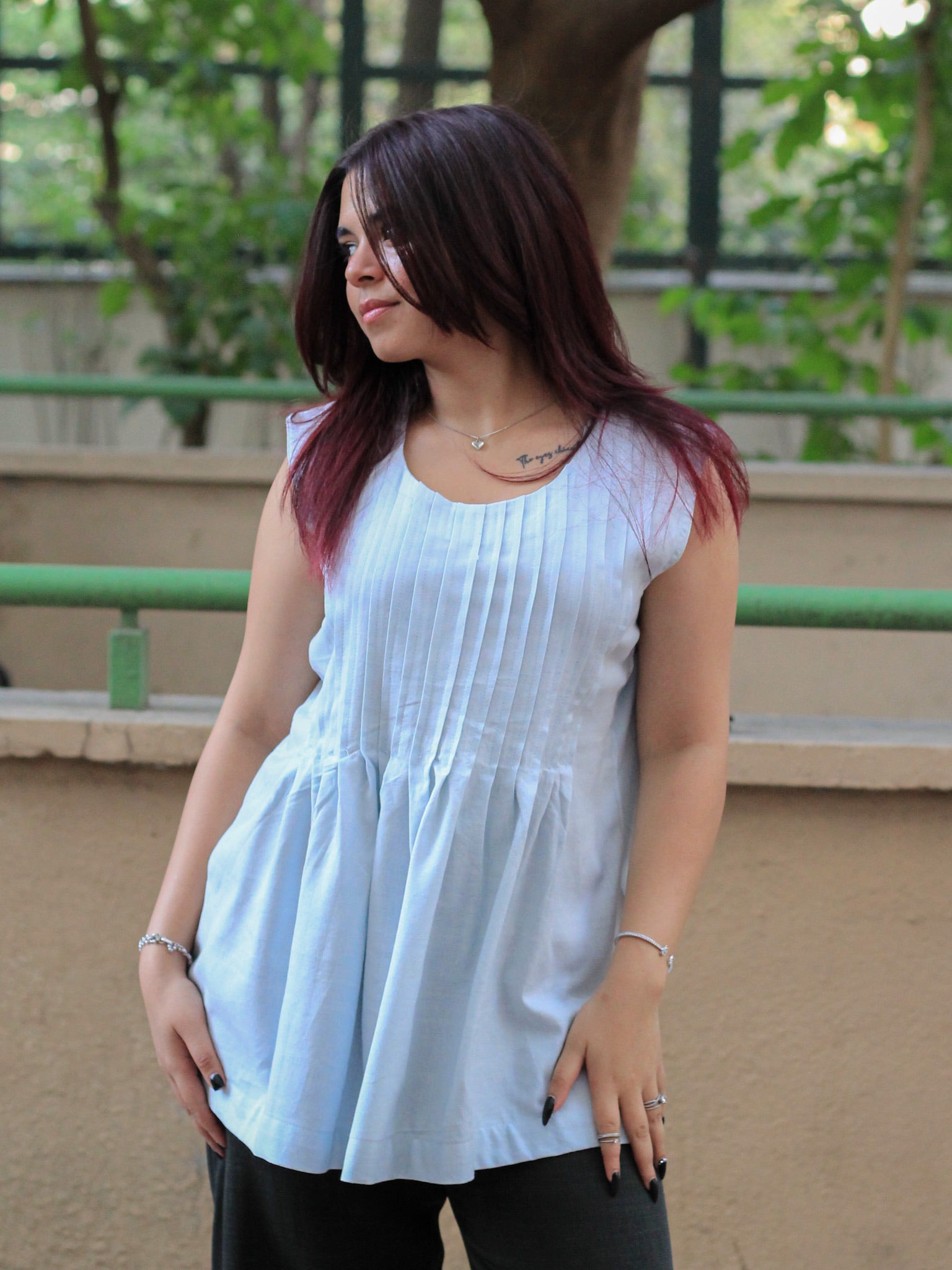 Model wearing Evara’s Skyline Haze Sleeveless Pleated Top, crafted from a sustainable blend of banana fiber and cotton. This airy light blue top features a sleeveless design, fine vertical pleats on the bodice, and a softly flared hem that offers a relaxed yet refined silhouette. Perfect for warm-weather layering or standalone elegance, it blends comfort with conscious fashion. Designed for consumers who value eco-friendly fabrics and contemporary, timeless style. Shop clothing at Evara.