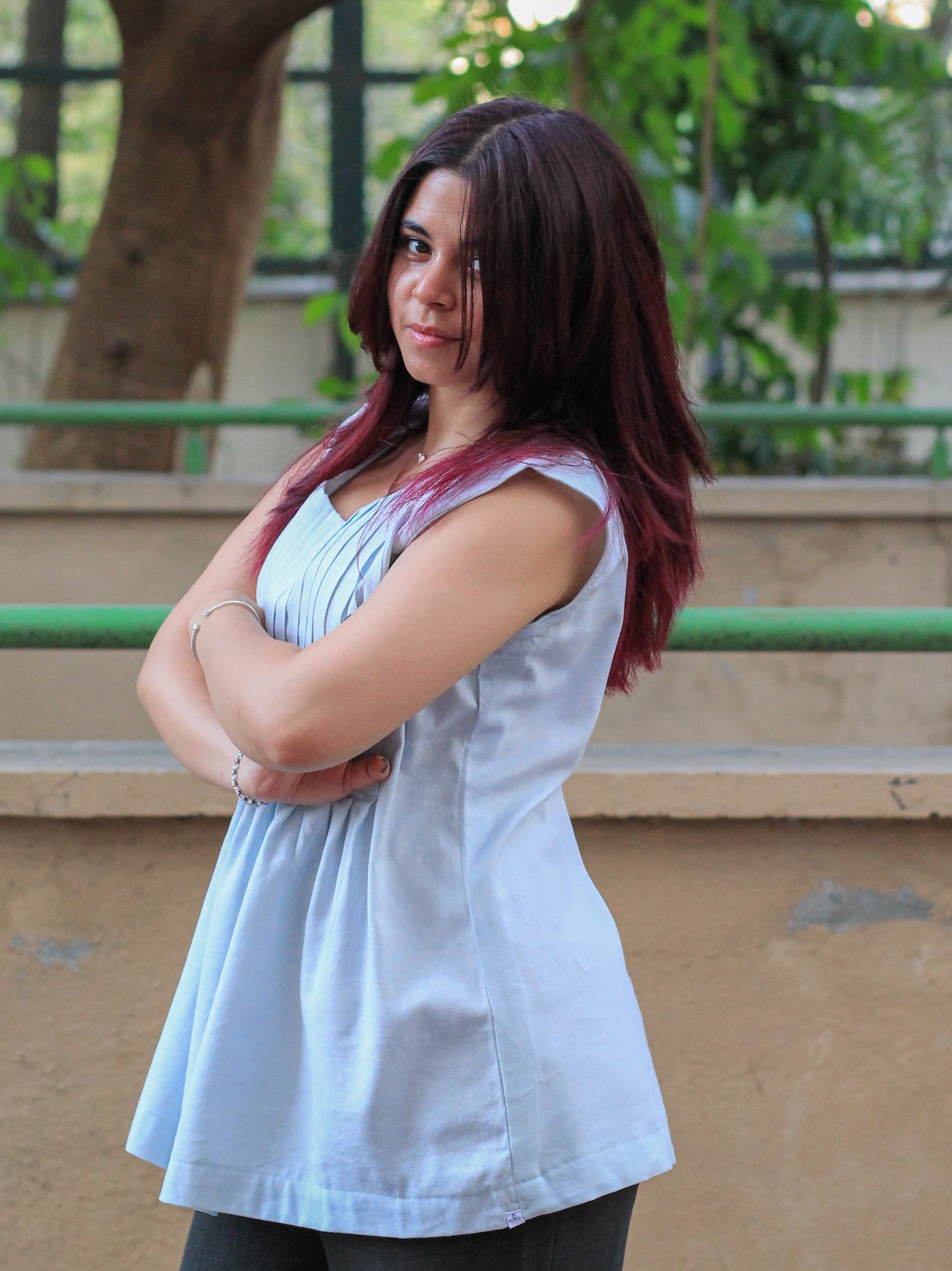 Model wearing Evara’s Skyline Haze Sleeveless Pleated Top, crafted from a sustainable blend of banana fiber and cotton. This airy light blue top features a sleeveless design, fine vertical pleats on the bodice, and a softly flared hem that offers a relaxed yet refined silhouette. Perfect for warm-weather layering or standalone elegance, it blends comfort with conscious fashion. Designed for consumers who value eco-friendly fabrics and contemporary, timeless style. Shop clothing at Evara.