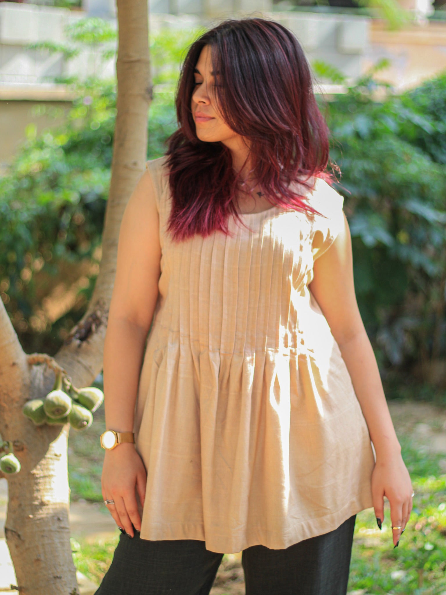 Model wearing Evara’s Dune Mist Sleeveless Pleated Top, crafted from a sustainable blend of banana fiber and cotton. This airy light blue top features a sleeveless design, fine vertical pleats on the bodice, and a softly flared hem that offers a relaxed yet refined silhouette. Perfect for warm-weather layering or standalone elegance, it blends comfort with conscious fashion. Designed for consumers who value eco-friendly fabrics and contemporary, timeless style. Shop clothing at Evara.