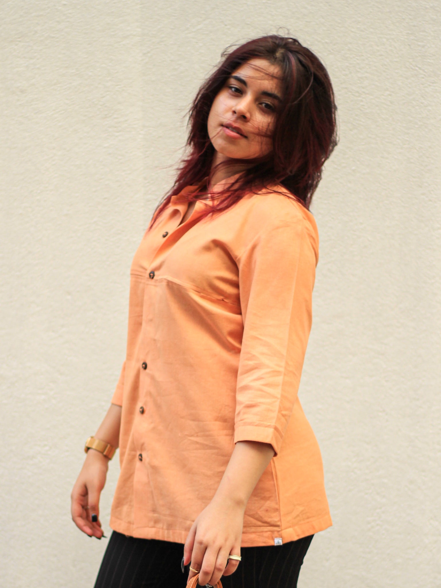Model wearing Evara’s Coral Dusk Button-Down Shirt, crafted from a premium blend of banana fiber and cotton. This elegant three-quarter sleeve shirt in a warm coral hue features a mandarin collar, a structured yet relaxed fit, and a stylish button-down front. Designed for effortless versatility, it pairs perfectly with both formal and casual looks. Designed for consumers who appreciate natural fabrics and timeless fashion. Shop clothing at Evara.